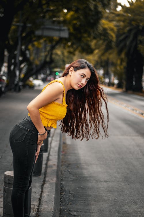 Young Woman in a Yellow Top Standing on the Sidewalk 