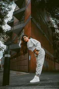 A fashionable young woman poses on an urban sidewalk in stylish streetwear.