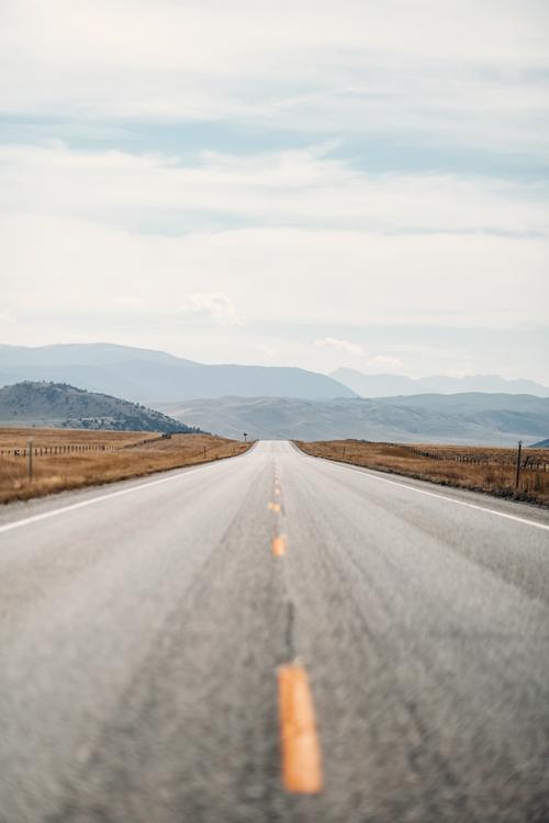 Free A serene rural road stretching towards distant hills under a cloudy sky, ideal for travel and adventure themes. Stock Photo