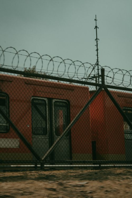 Free An urban train passing behind a barbed wire fence during the day. Stock Photo