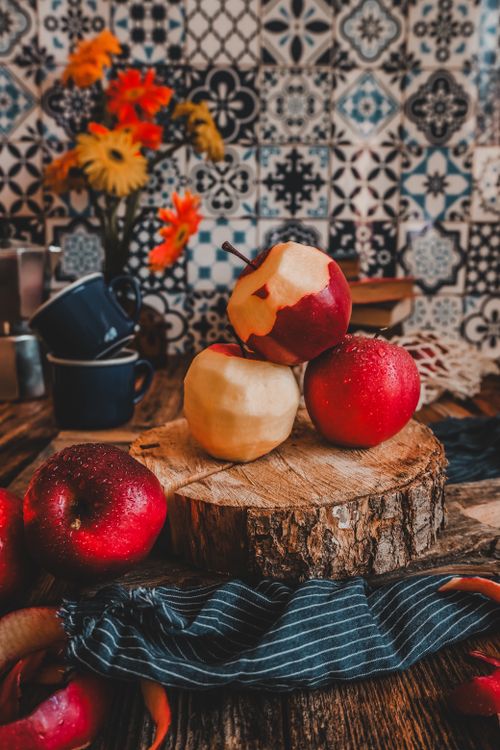 Free Peeled and unpeeled apples on a wooden stump with a cozy kitchen backdrop. Stock Photo