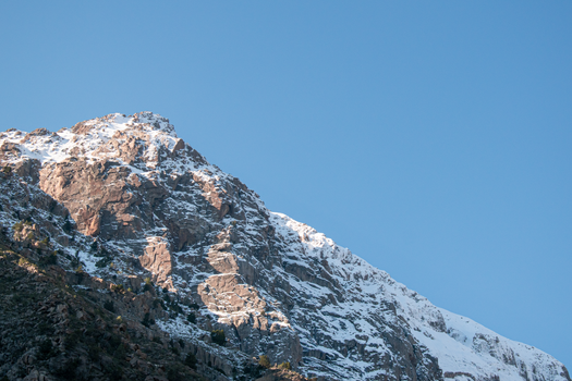 A high rocky mountain peak with snow under a clear blue sky, showcasing winter's beauty.