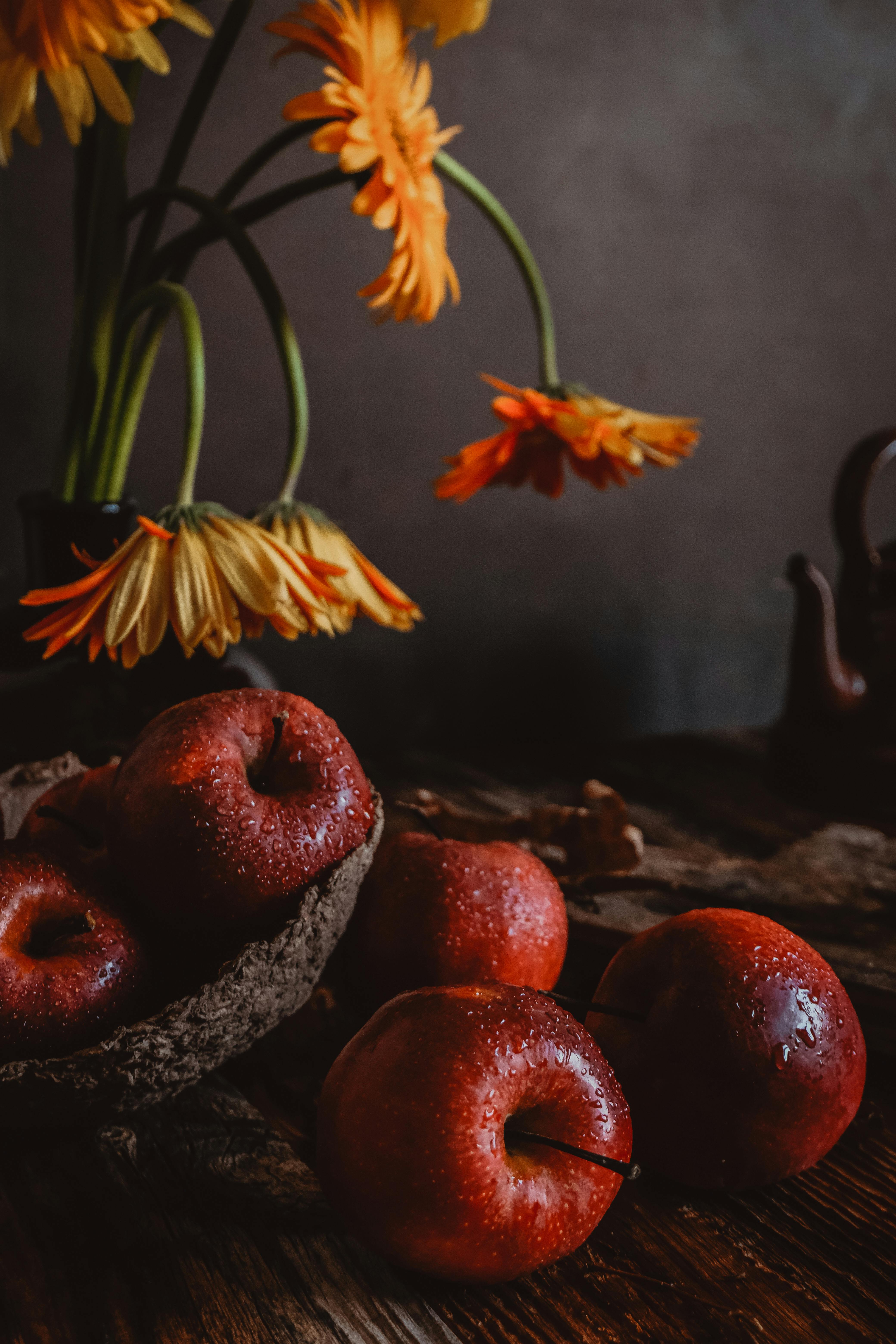 Moody still life of red apples and yellow flowers on a wooden table.