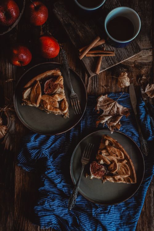 Free Delicious apple pie slices on rustic table with apples, cinnamon sticks, and coffee cups, perfect for fall. Stock Photo