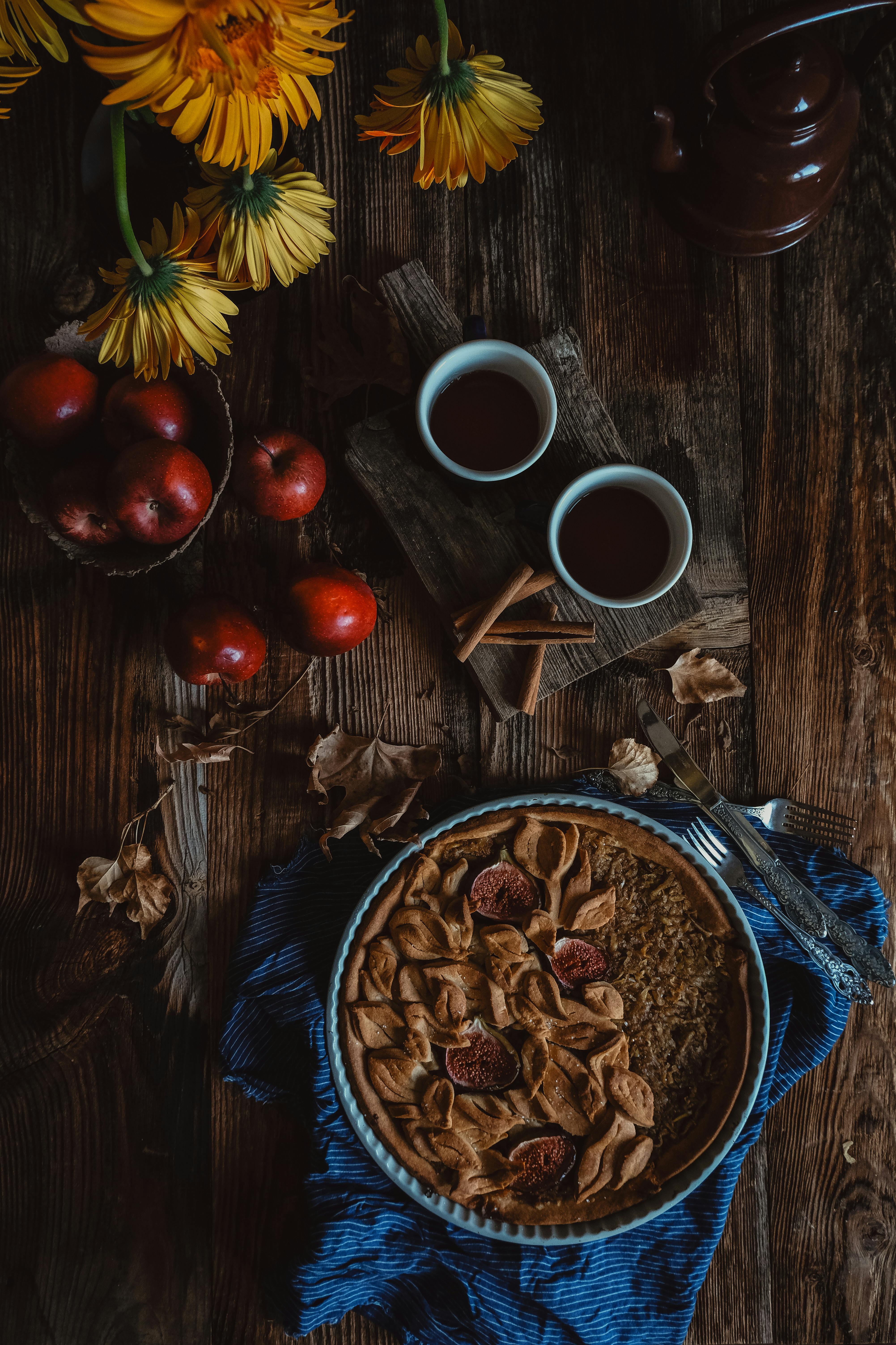 Flat lay of a rustic table with apple fig pie, tea cups, and autumn decor.