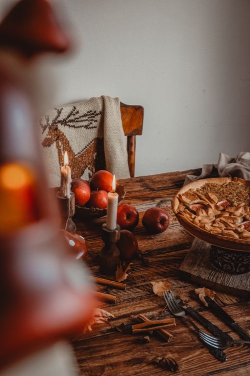 Free Warm autumn setting with apple pie, candles, apples, and rustic decor for a cozy indoor ambiance. Stock Photo