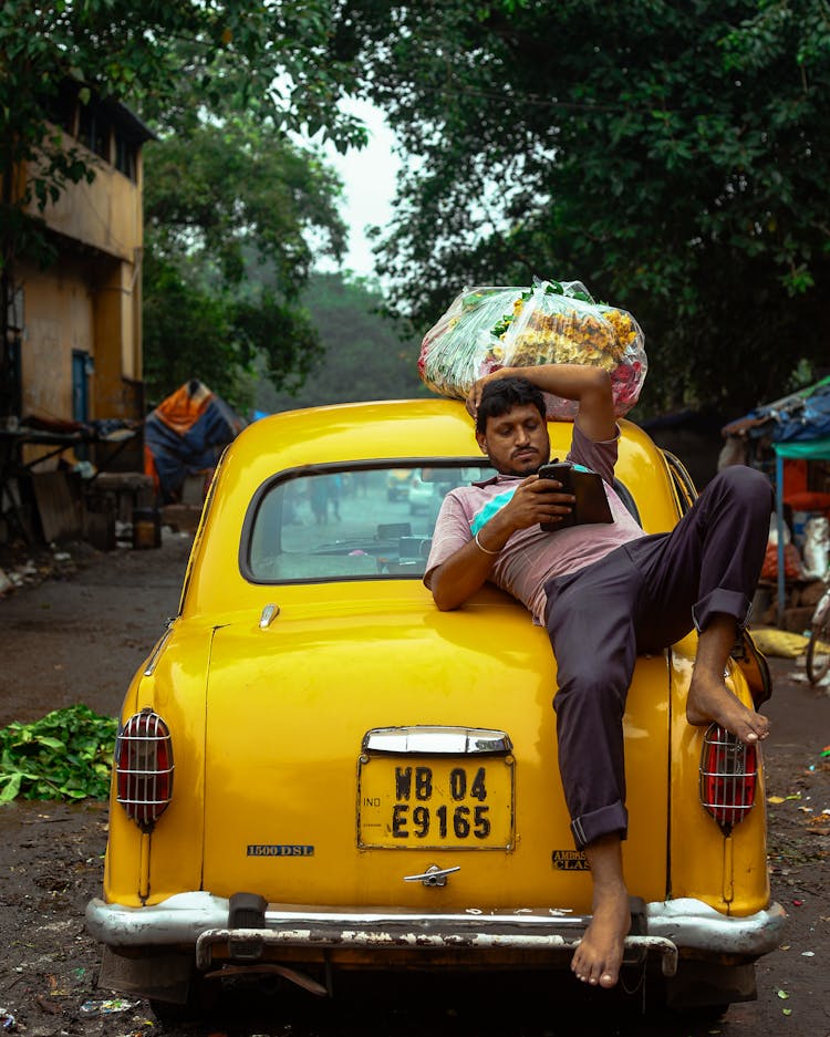 Man Lying On Car Hood With Cellphone