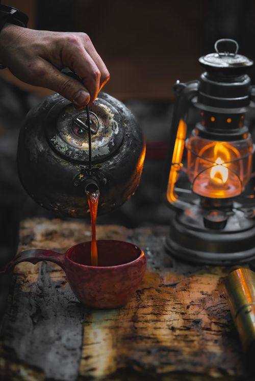 Free A hand pours tea from a vintage kettle beside an antique lantern, creating a cozy atmosphere. Stock Photo