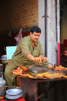 A man cooking traditional street food on a large griddle in an outdoor market.