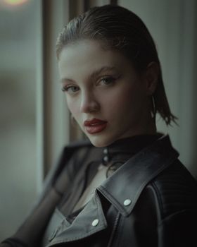 Stylish portrait of a woman in a leather jacket looking outside.