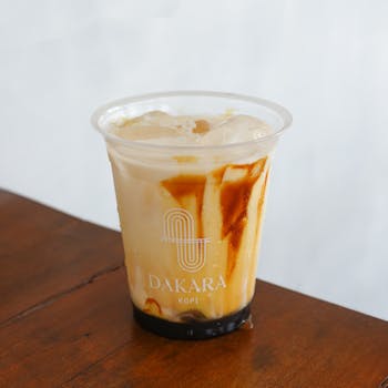 Refreshing iced coffee in Dakara Kopi cup with caramel swirls on wooden table in Yogyakarta.