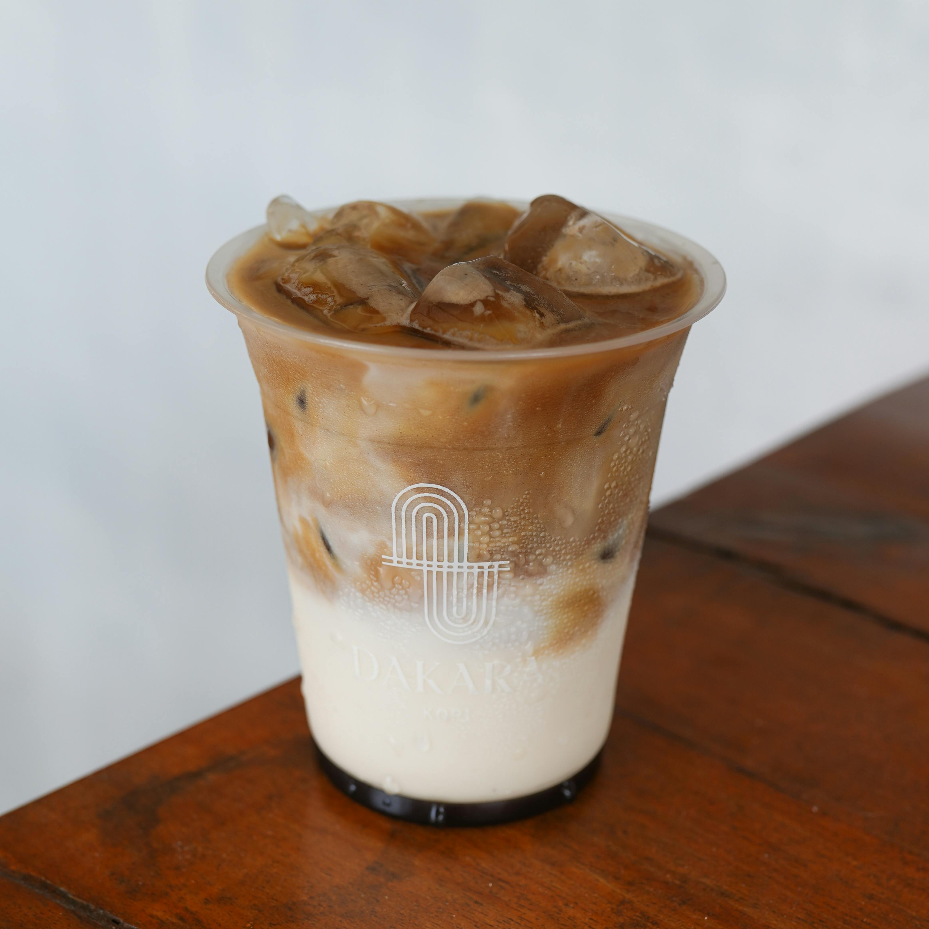 Delicious iced coffee latte served in a transparent cup with ice cubes on a wooden table.