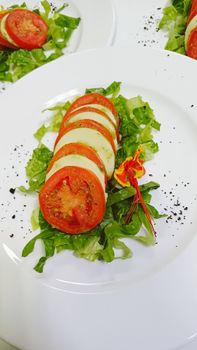 Delicious fresh Caprese salad with tomatoes, mozzarella, and edible flowers on a bed of lettuce.