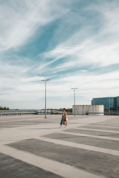 Free Stylish woman walking in an empty urban parking lot under a bright sky. Stock Photo