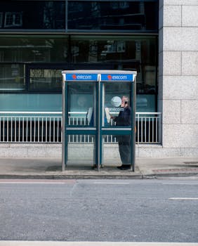A man makes a call from a classic phone booth on a Dublin street, offering a glimpse into urban life.
