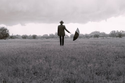 Elegant Man with Umbrella Standing Alone on Meadow