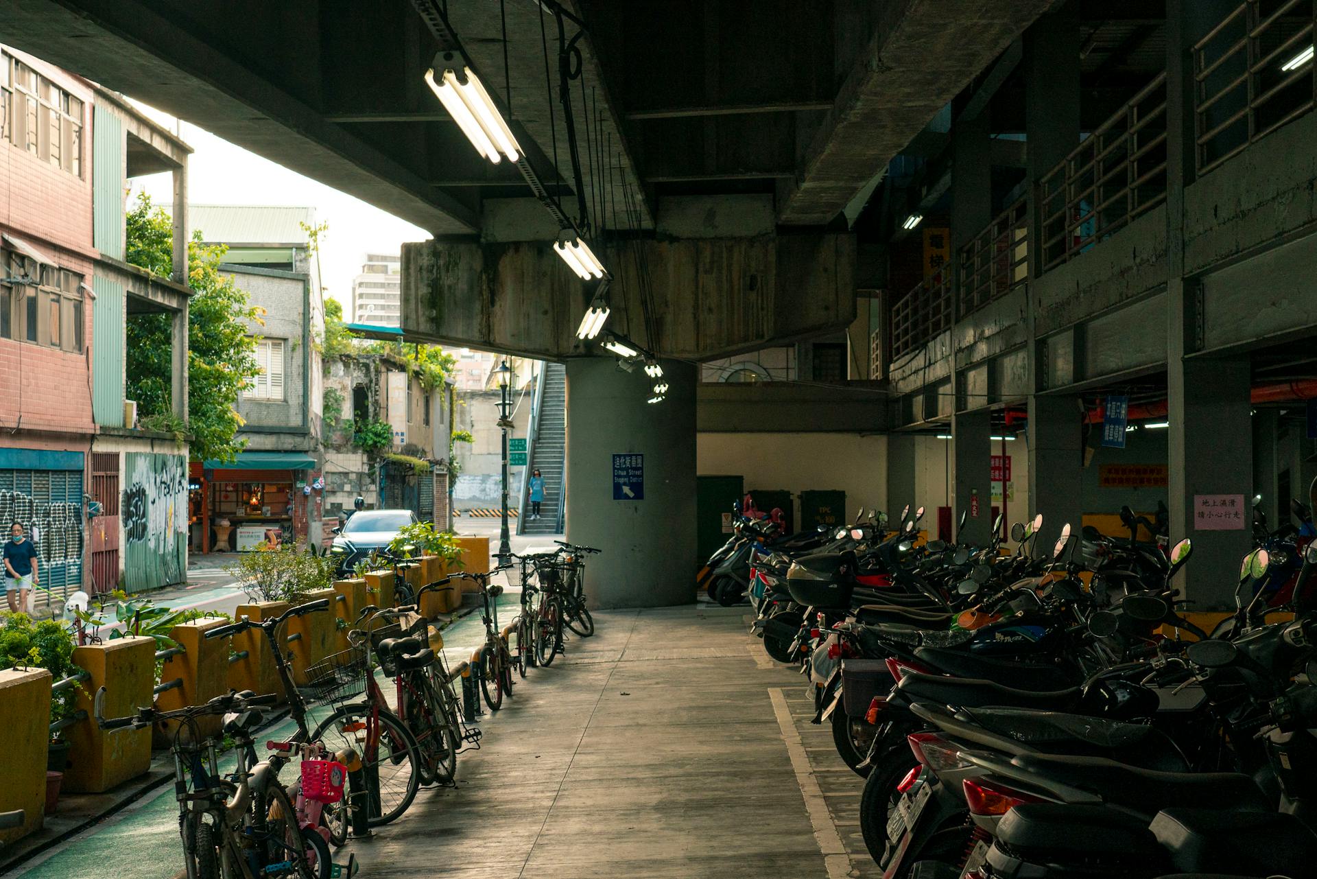 A lively urban street with parked bicycles and motorcycles under an overpass.