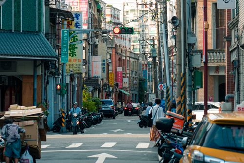 Free A busy city street scene with motor scooters, cars, and pedestrians in an urban setting. Stock Photo
