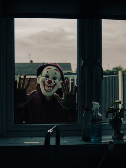 Free A frightening clown mask seen from indoors, creating a spooky Halloween atmosphere. Stock Photo