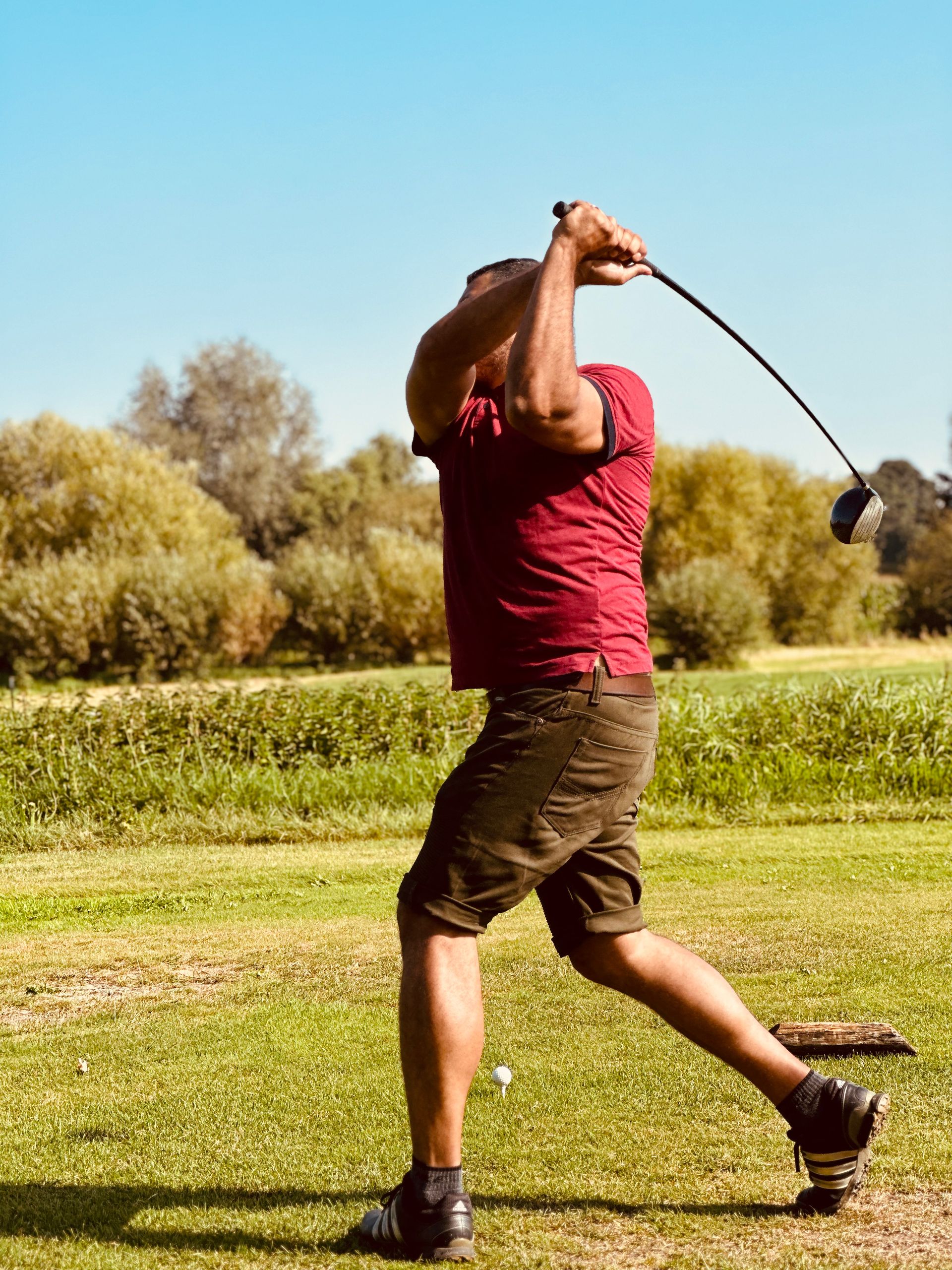 Golfer in a red polo mid-swing on the fairway at golden hour