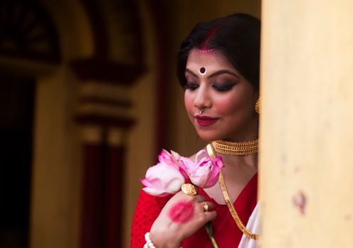 Gorgeous Indian woman in traditional attire holding pink lotus flowers in Kolkata, India.