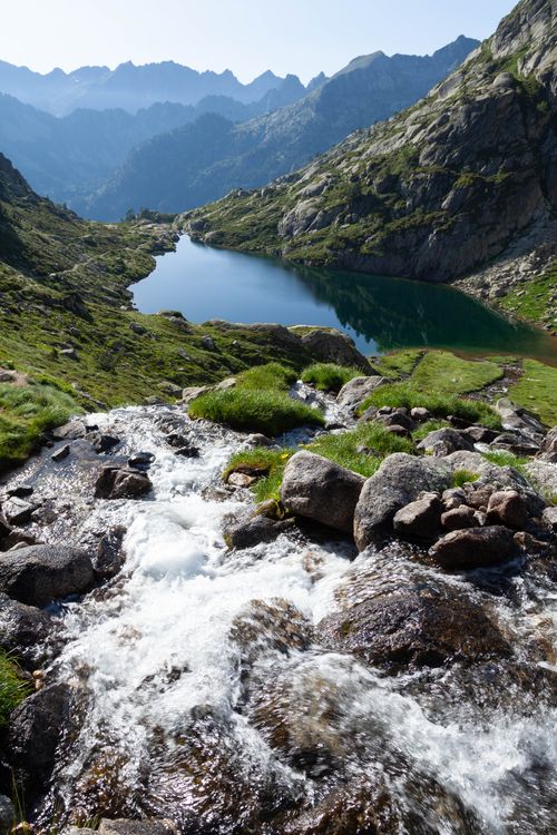 Free Discover the serene beauty of Cauterets with a tranquil stream cascading into a peaceful lake amid majestic mountains. Stock Photo