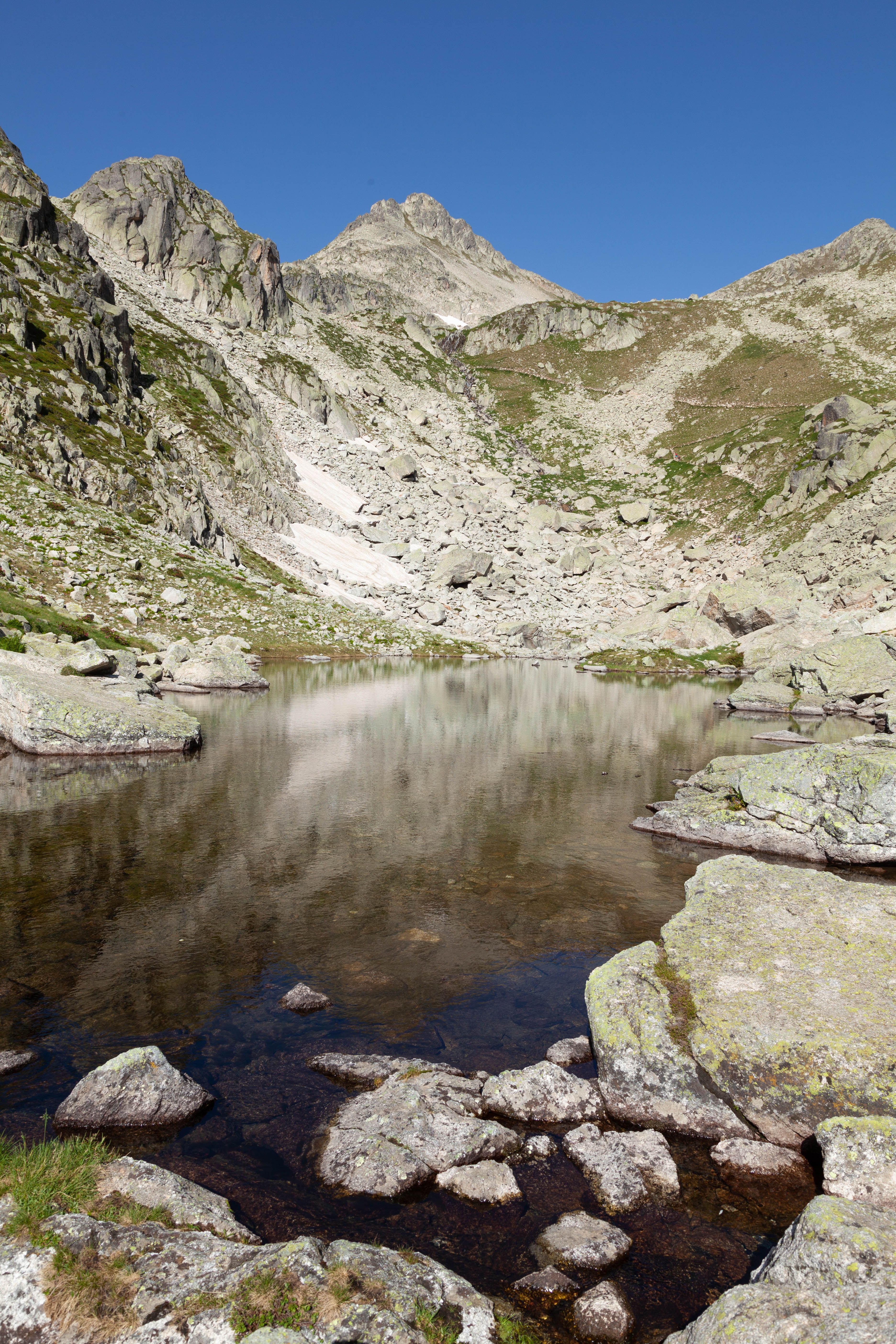 A mountain lake surrounded by rocks and grass · Free Stock Photo