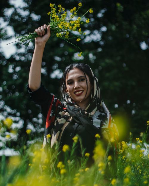 Free Middle Eastern woman smiling and holding a yellow bouquet in a vibrant meadow. Stock Photo