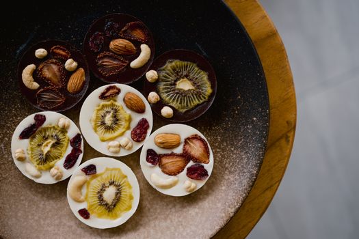A visually enticing platter of chocolate circles topped with fruits and nuts, a perfect gourmet treat.