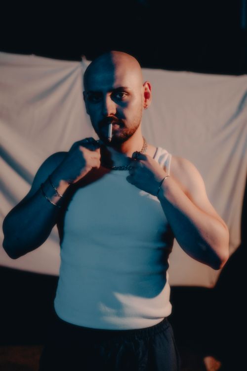 Free A bald man stands confidently at night, smoking in a tank top. Stock Photo
