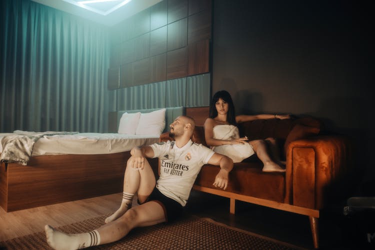 Man In Real Madrid Jersey Sitting On Floor And Woman Sitting On Couch Behind