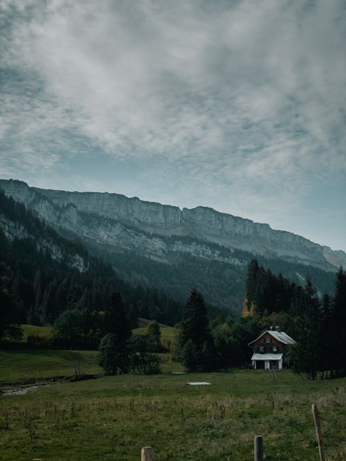 A serene view of an alpine mountain range with a solitary cabin nestled in a grassy field.