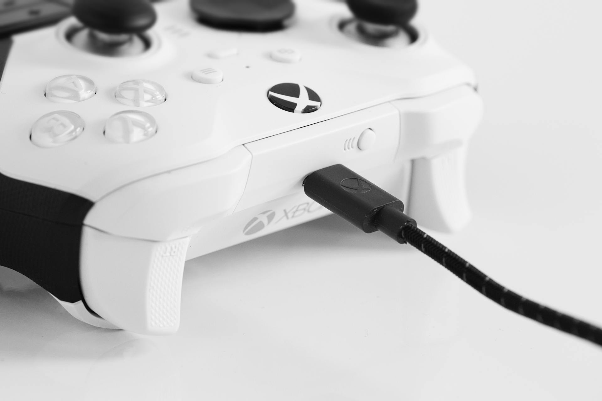 High-quality black and white photo of a charging Xbox controller, featuring modern design.