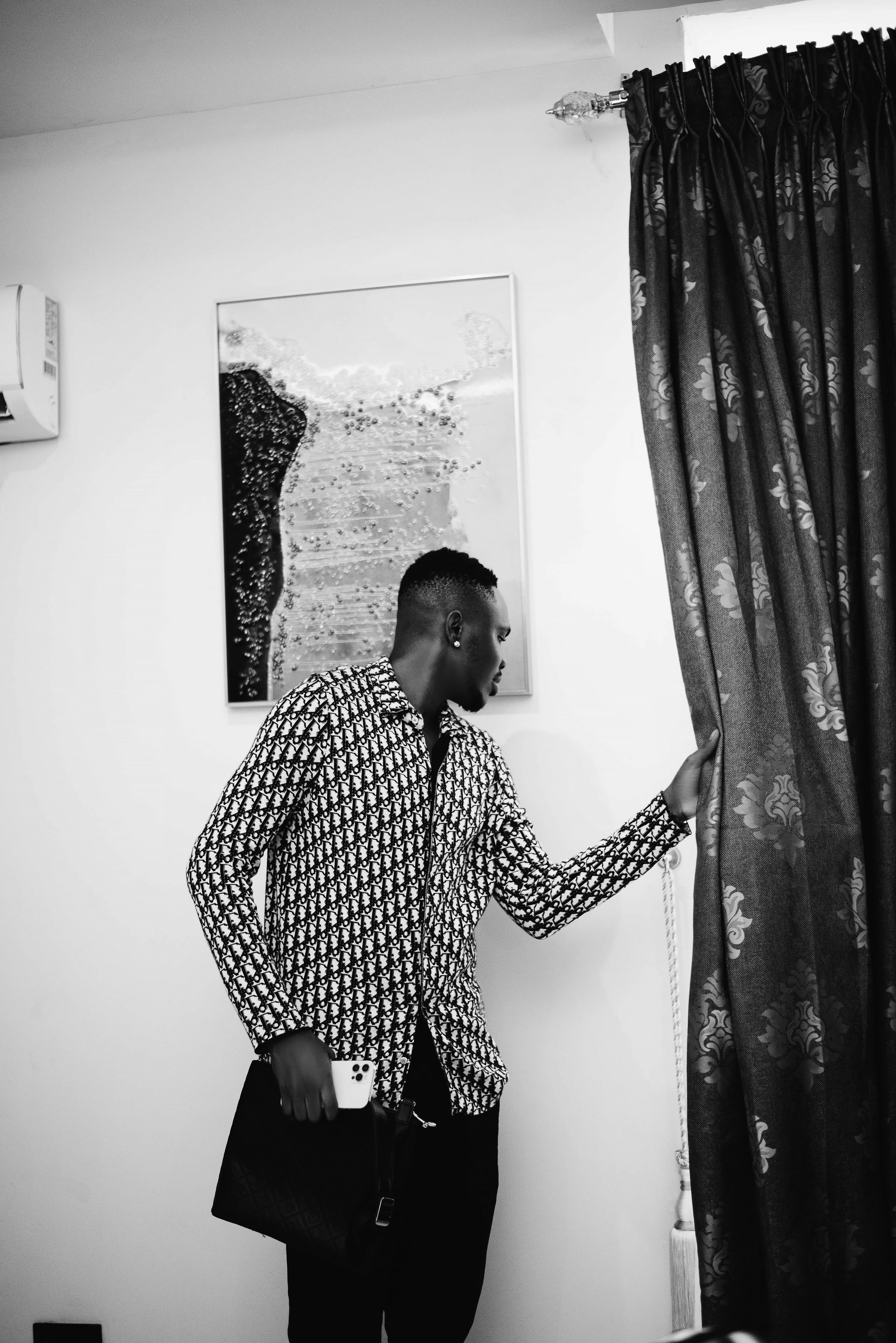 Stylish black and white portrait of a man standing by a curtain, exuding elegance.