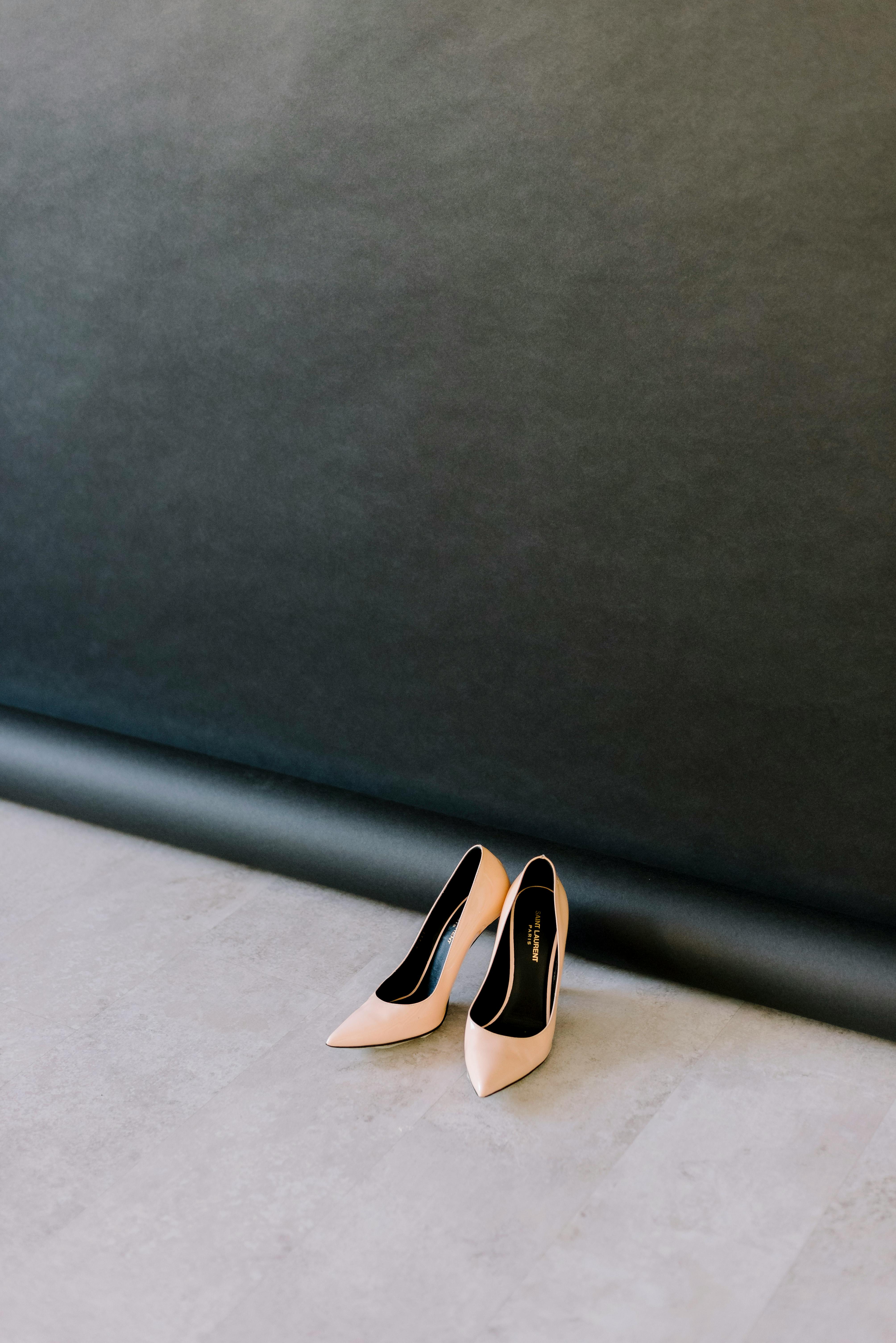 A pair of nude high heel shoes placed on a smooth floor with a minimalist dark backdrop, highlighting fashion elegance.