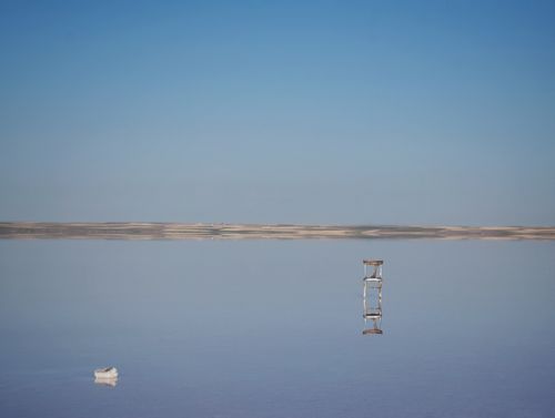 Free A solitary chair reflects on a calm salt flat under a clear blue sky, creating a serene scene. Stock Photo