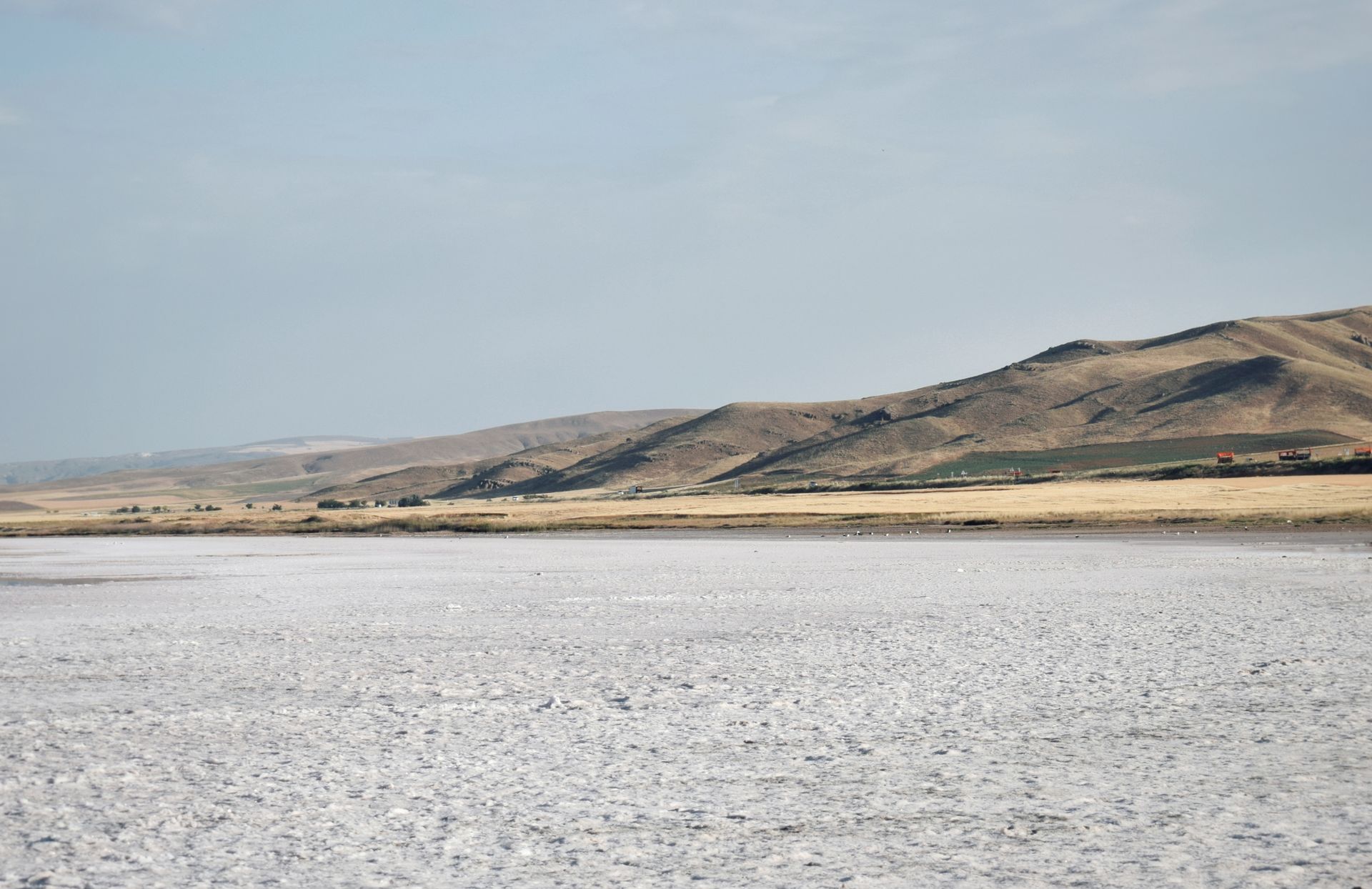 Peaceful view of a salt lake with barren hills in a rural landscape under a clear sky.