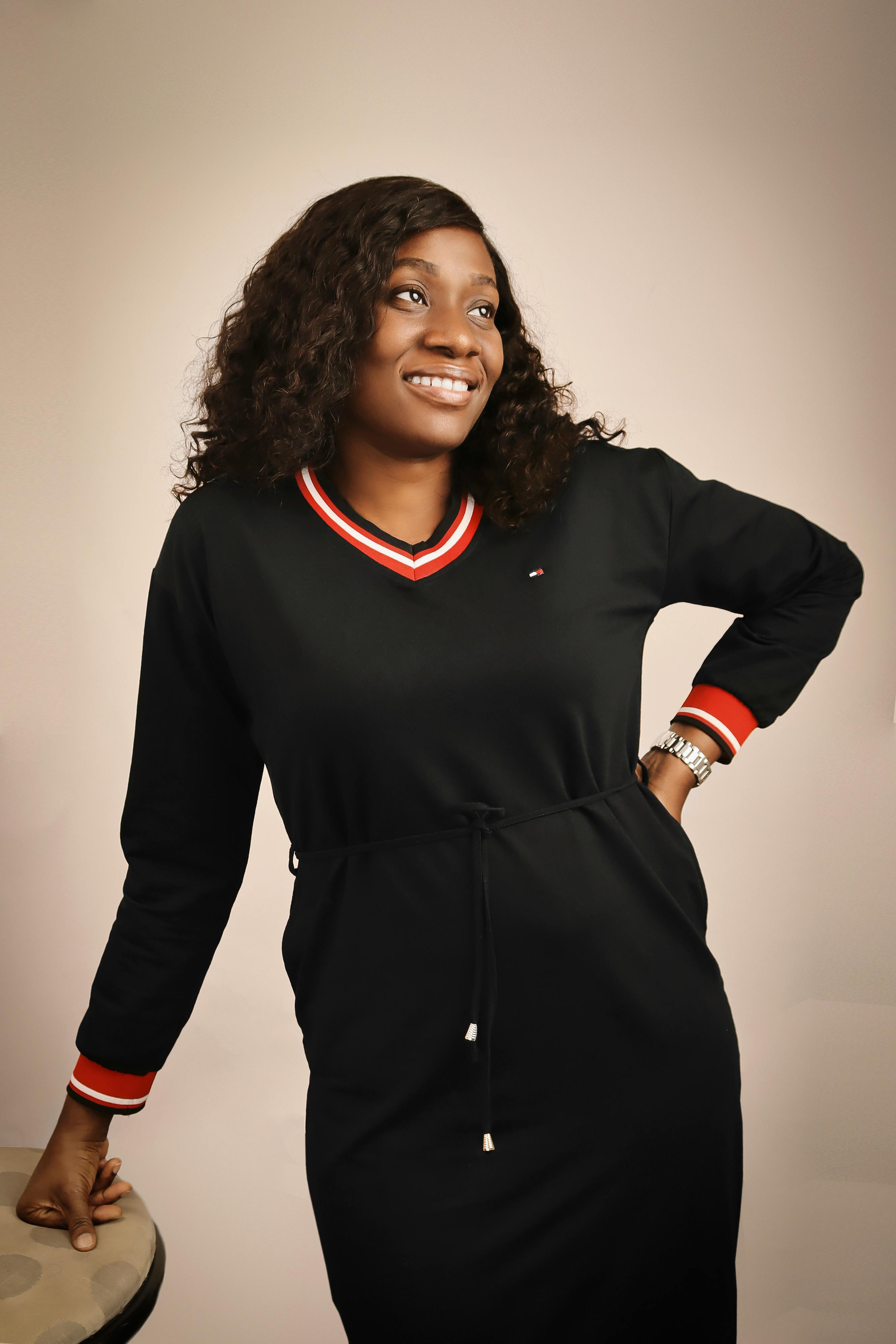 Portrait of a smiling woman in a black dress captured indoors with a warm, fashion-forward vibe.