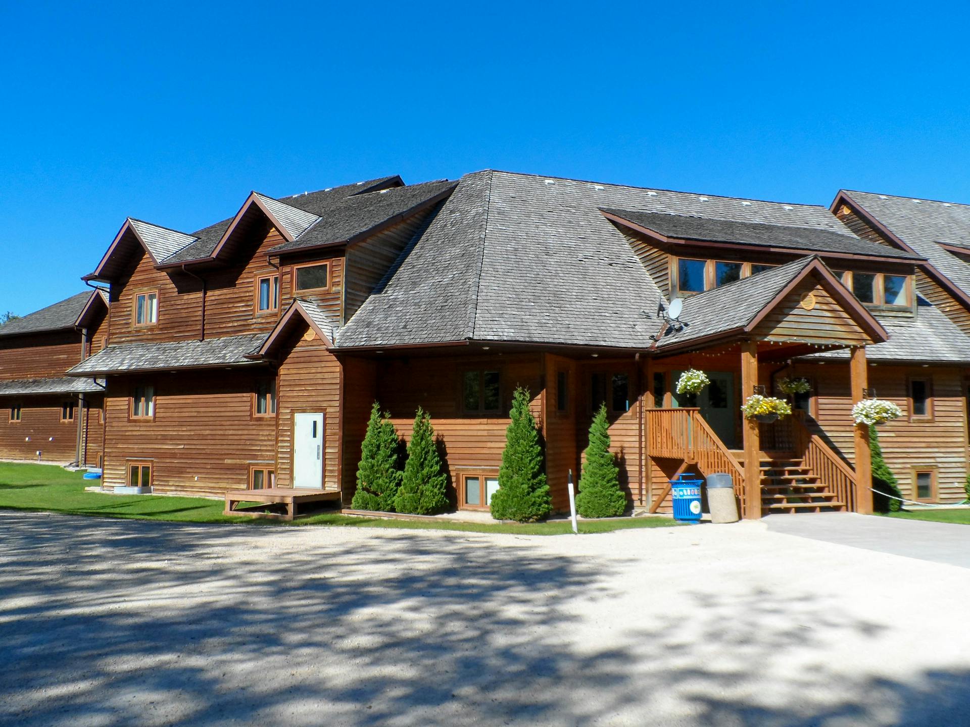 Beautiful two-story wooden house with gabled roof and lush greenery under a vibrant blue sky.