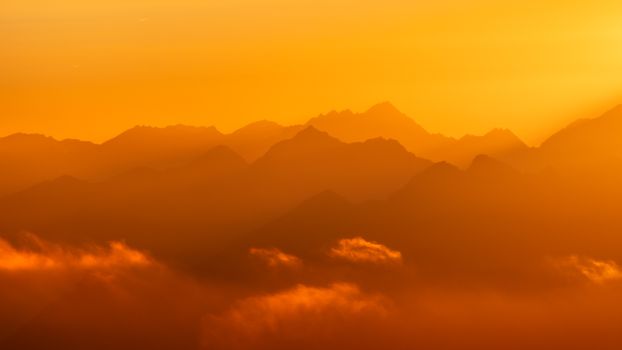 Majestic silhouette of mountain peaks at sunset with vibrant orange hues.