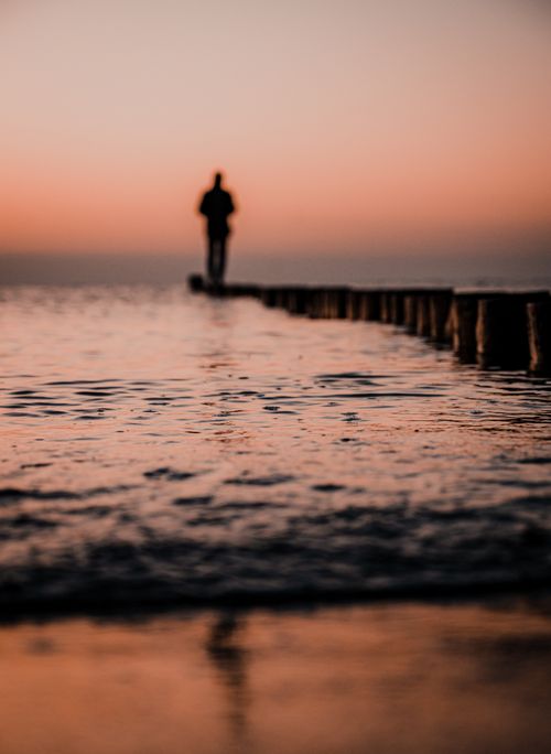 Free A lone silhouette standing on a breakwater at the beach during a vibrant sunset. Stock Photo