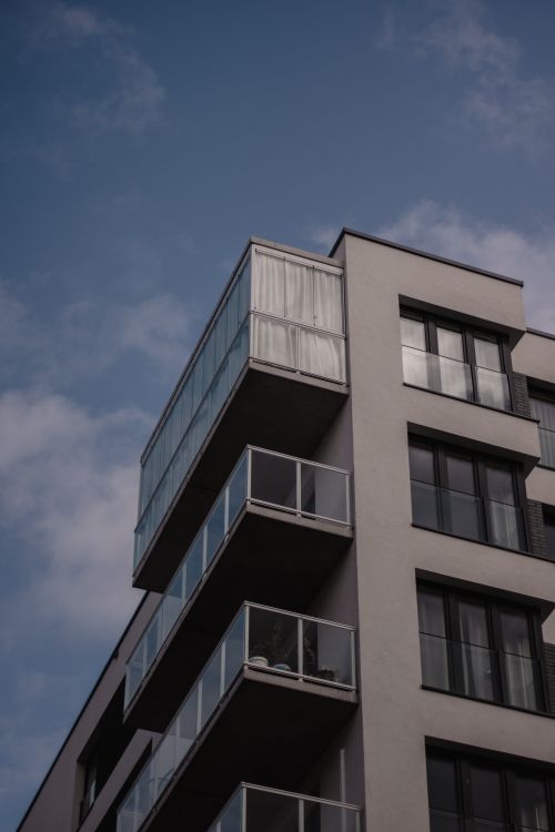 Free A modern residential building with sleek glass balconies against a clear sky. Stock Photo