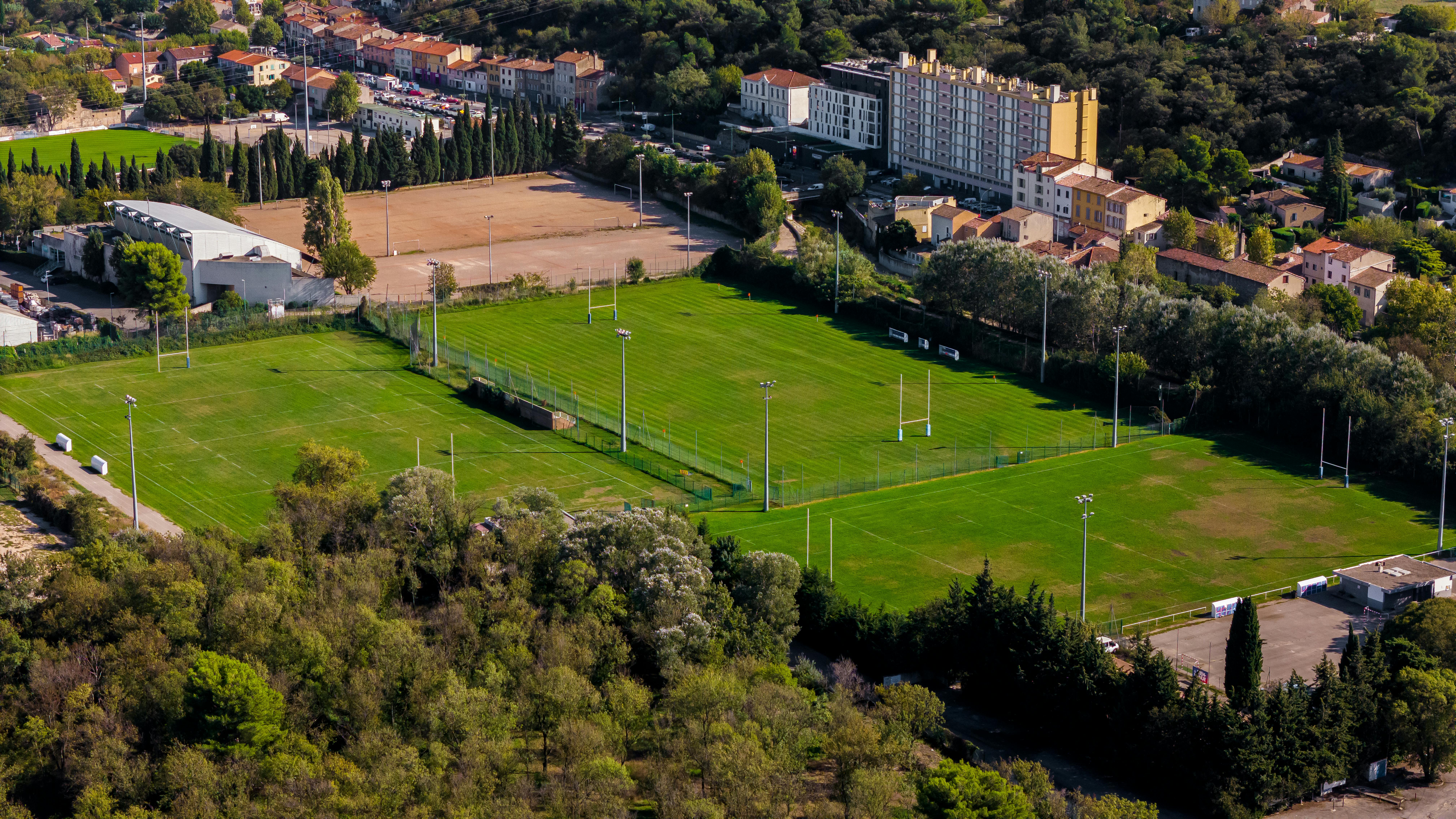 Aerial shot of lush green soccer fields and urban area in Marseille, France.