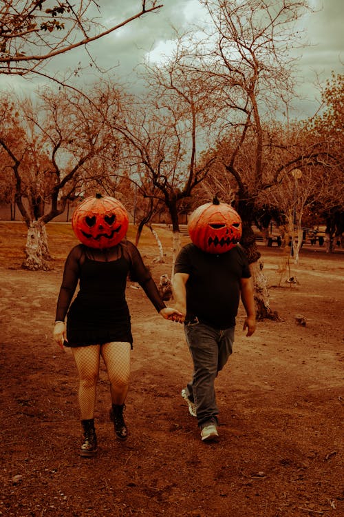 A Couple with Carved Pumpkins on Their Heads Walking and Holding Hands