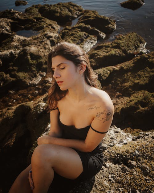 Young Woman in Black Mini Dress Sitting on a Rock by the Sea