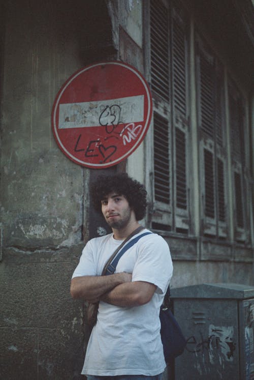 Young Man Standing beside a Road Sign on the Street in City 