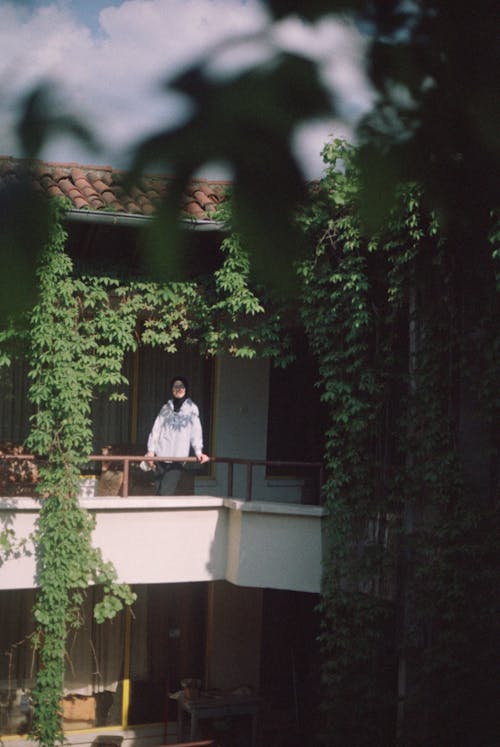 Woman Standing on a Balcony in a Building Covered with Ivy
