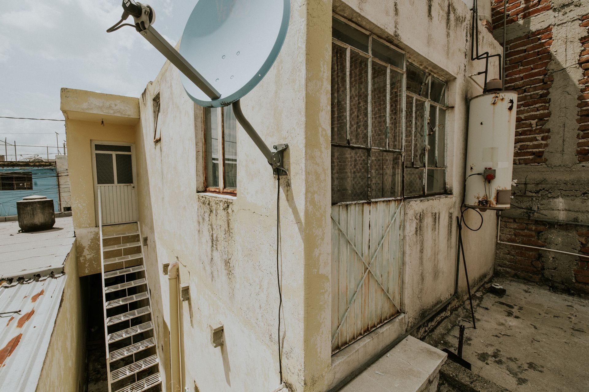 Old urban rooftop with satellite dish and metal staircase.