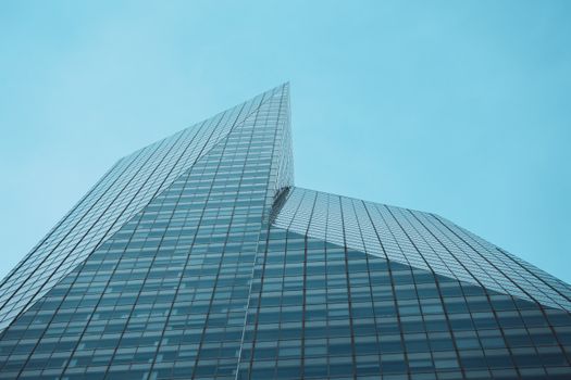 Contemporary skyscraper with glass facade shot from below against a clear blue sky.
