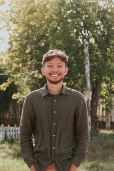 Smiling young man in a green shirt enjoying a sunny day outdoors in a lush garden.